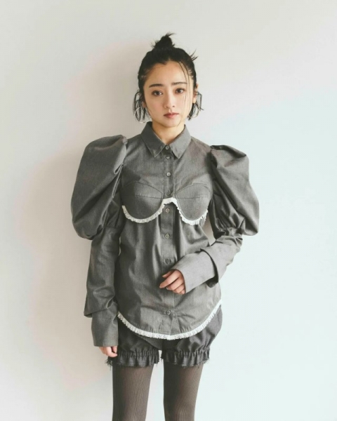 女性がグレーのシャツとショートパンツを着て立つスタイリング