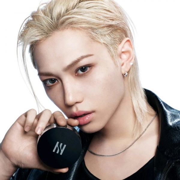 金髪の男性が黒いコンパクトを持ち、こちらを見ている写真。